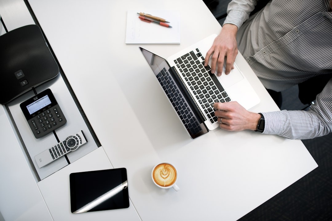 Persoon werkend op laptop aan een witte houten tafel, focus op digitaal werken